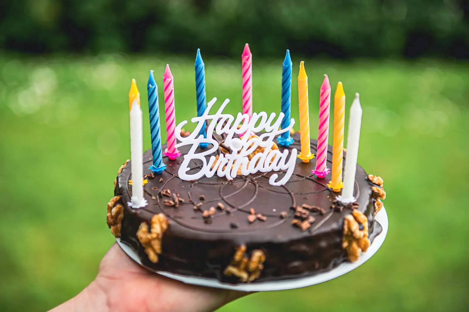 Birthday cake with candles held up on a green lawn