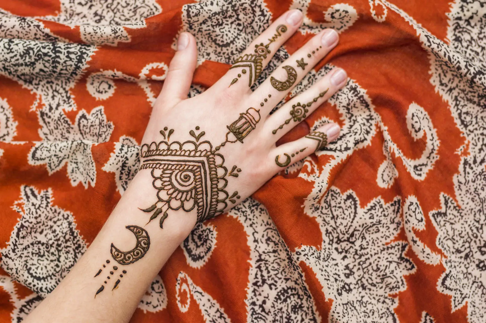 Intricate bridal henna design on hands resting on orange fabric