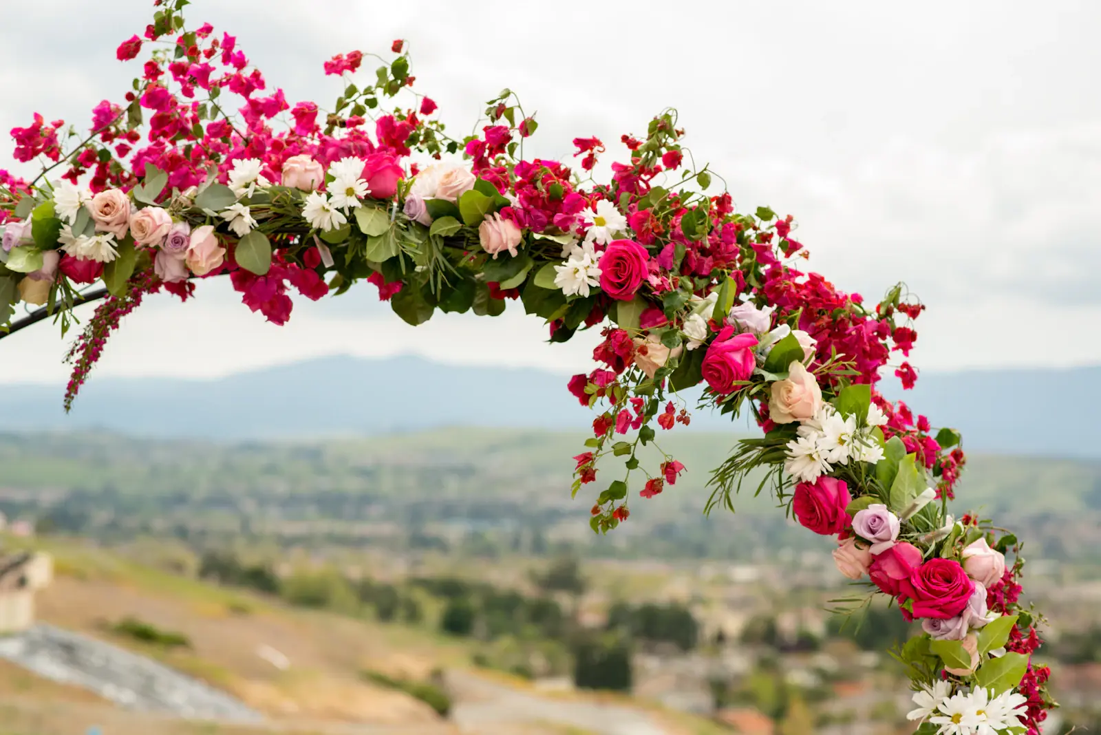 Pink floral wedding arch overlooking green hills