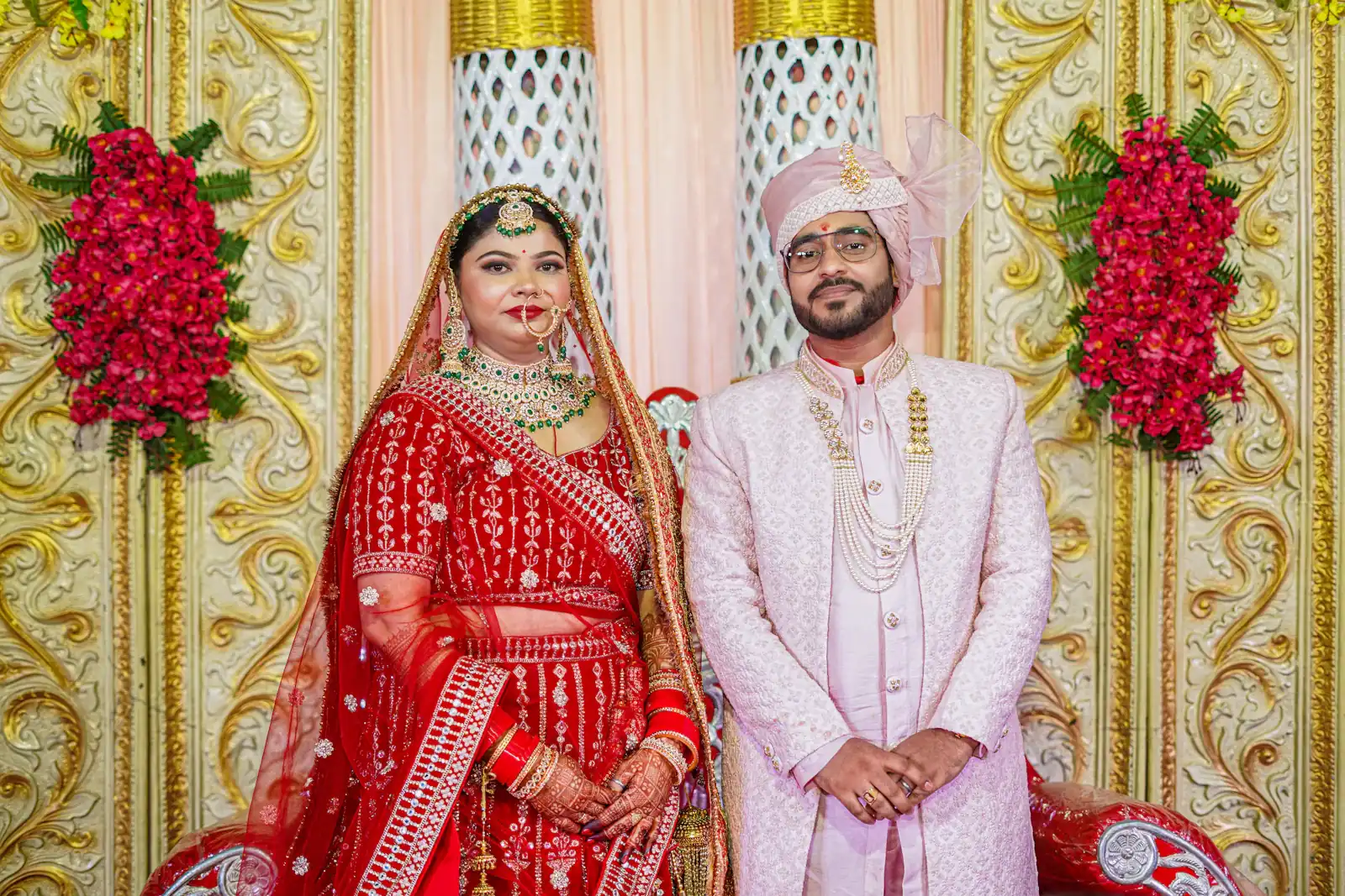Bride and groom in red and gold outfits on a floral stage