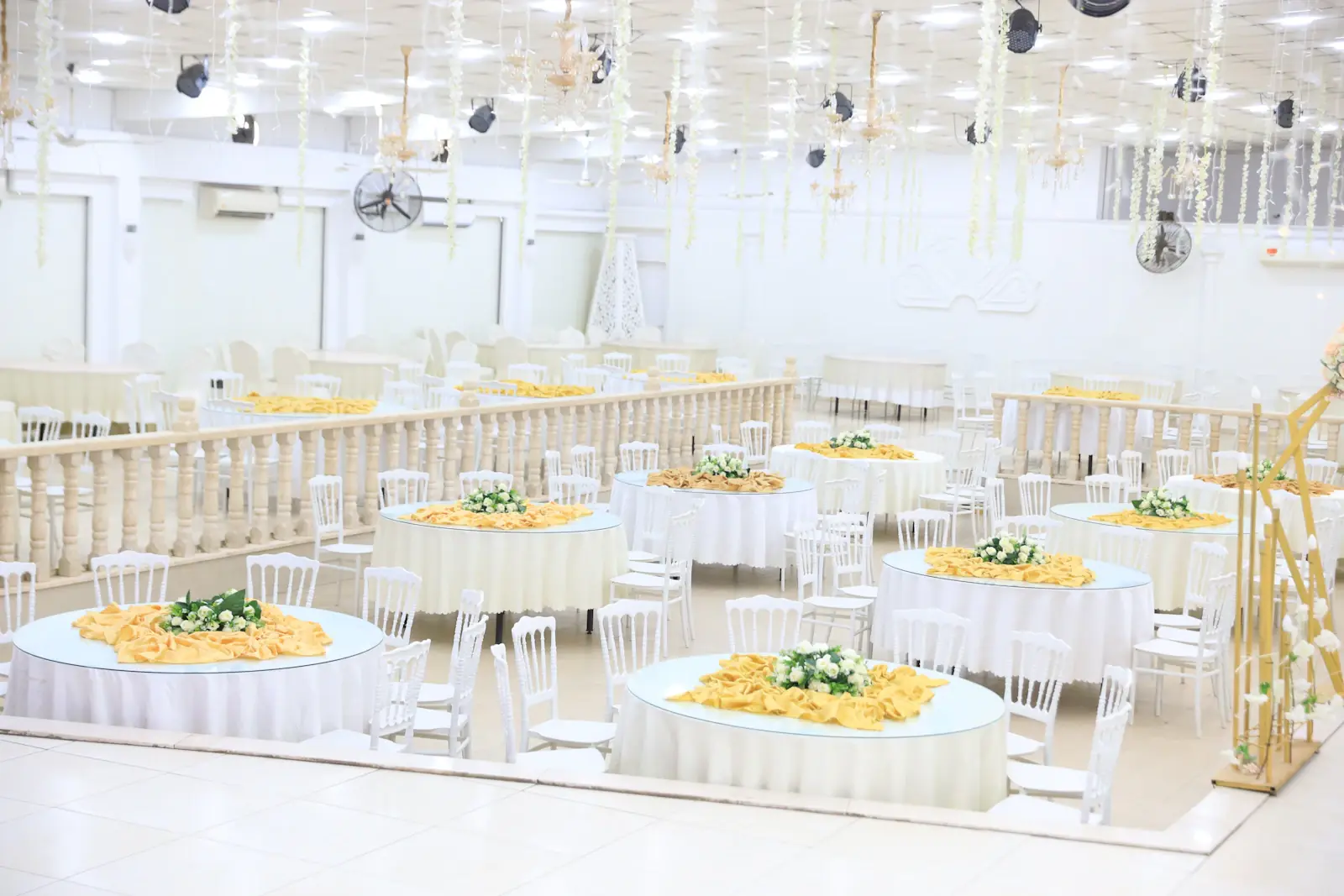 Venue Sourcing in Lahore - Bright white banquet hall with floral centerpieces on long tables